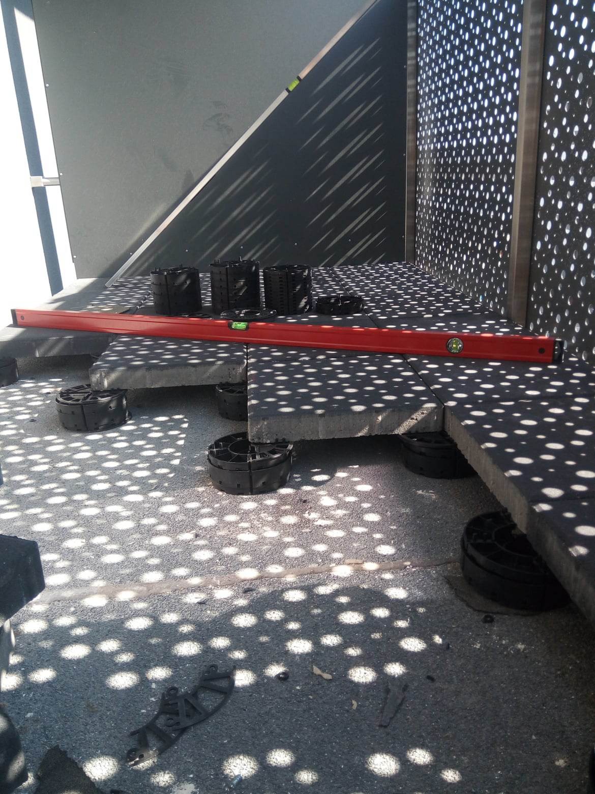 Taras wentylowany w trakcie montażu, płyty wsparte na regulowanych wspornikach, poziomowanie płyt za pomocą poziomicy, ażurowe ściany tworzą cień w kropki.