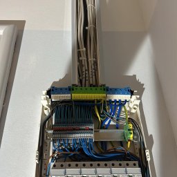Elektro-Automatic Marcin Michalak - Rozdzielnica elektryczna z licznymi przewodami w białej obudowie, widoczne zabezpieczenia topikowe i różnicowoprądowe marki Legrand, kable prowadzone w korytku pionowo do góry z numeracją na kablach.