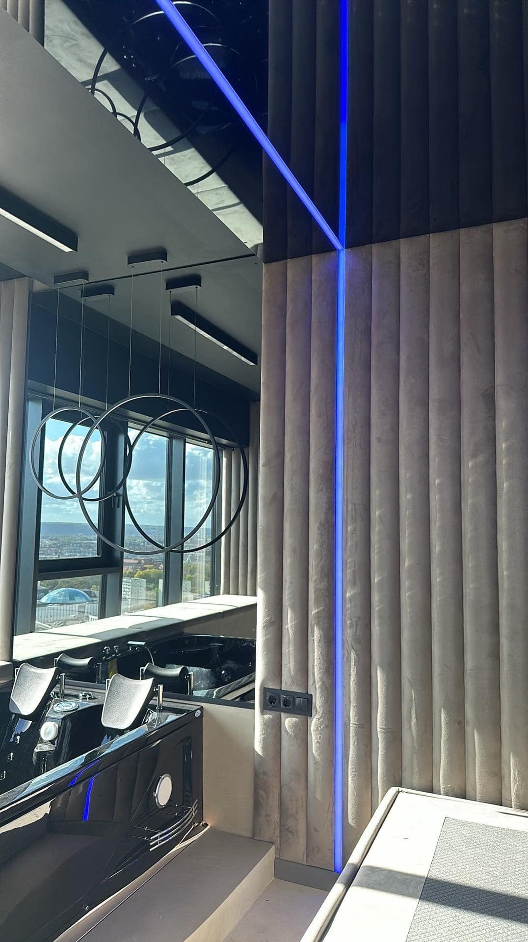 Nowoczesny salon kąpielowy z jacuzzi, oświetleniem LED w ścianie i designerską lampą wiszącą z okrągłych obręczy na tle panoramy miasta.