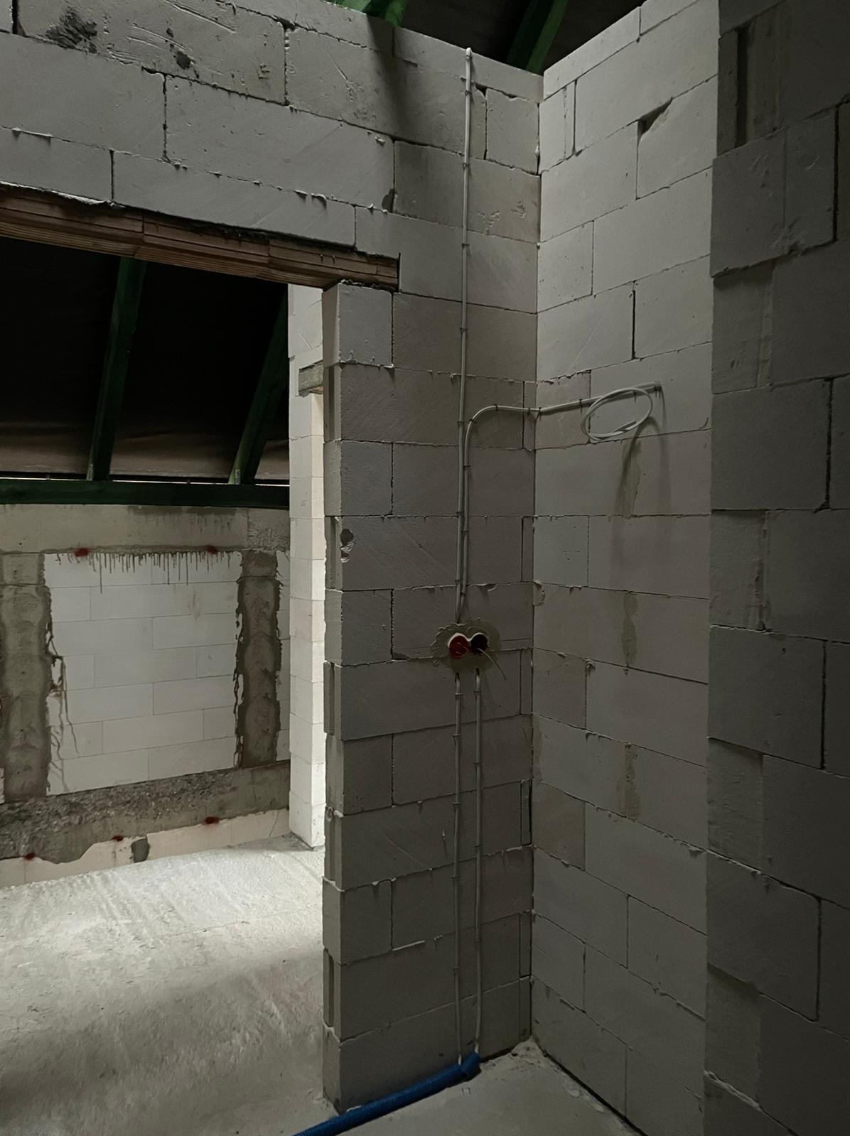 Wewnętrzne ściany z betonu komórkowego w trakcie budowy, widoczne pionowe kable elektryczne w peszlu, przygotowane punkty instalacji elektrycznej, surowy stan wykończenia.