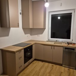 Usługi stolarskie Cezary - Beżowa kuchnia na wymiar z drewnianym blatem, widok na zabudowę z piekarnikiem, płytą indukcyjną i zlewem. Na blacie leżą narzędzia.