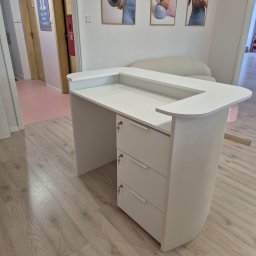 Usługi stolarskie Cezary - Biała lada recepcyjna z trzema szufladami na klucz, widoczna na tle jasnego wnętrza z elementami dekoracyjnymi i drewnianą podłogą.