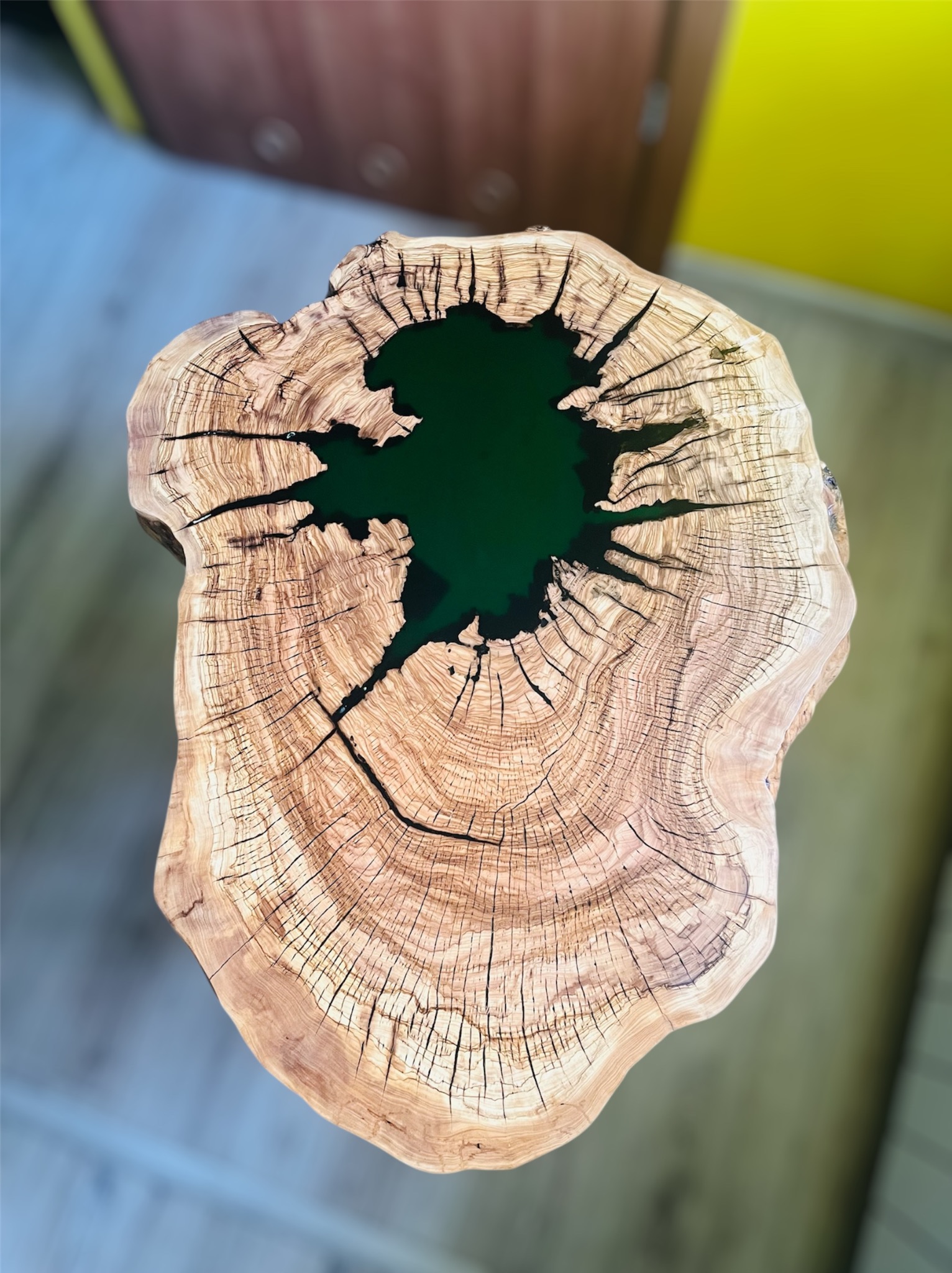 Unikatowy stolik kawowy z plastra drewna z żywicą epoksydową w kolorze butelkowej zieleni, ukazujący naturalne słoje i pęknięcia drewna. Widok z góry.