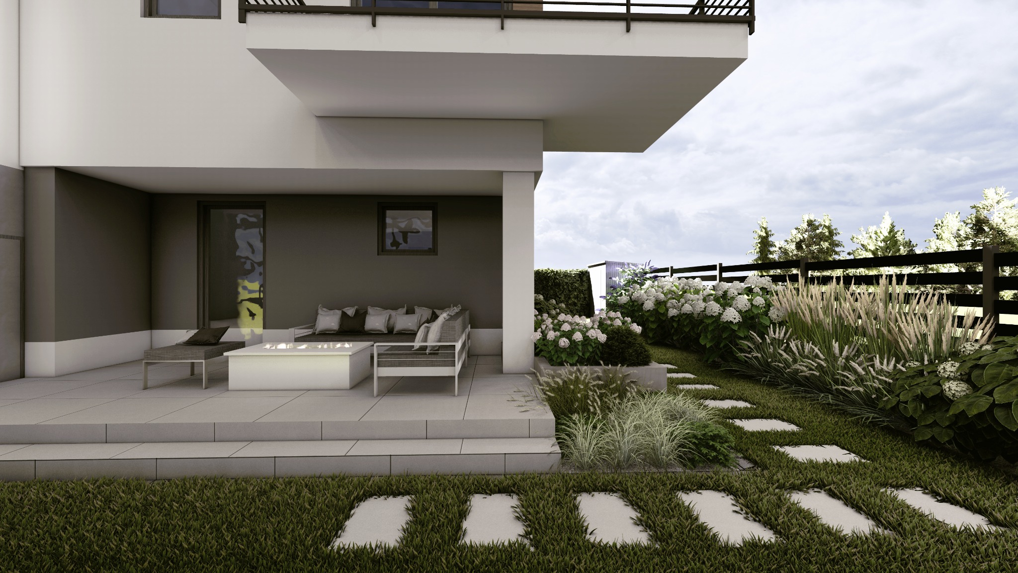 Nowoczesny taras z białymi meblami wypoczynkowymi i paleniskiem gazowym, otoczony ścieżką z płyt w trawie i rabatami z hortensjami oraz trawami ozdobnymi, widok na czarne ogrodzenie i drzewa w tle.