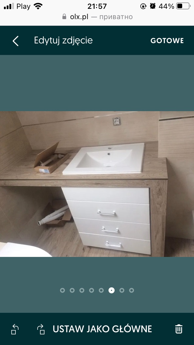 Biała umywalka nablatowa z czterema szufladami w łazience, widoczne rury w kartonie, gniazdko elektryczne na ścianie, imitacja drewna na blacie i bokach szafki.