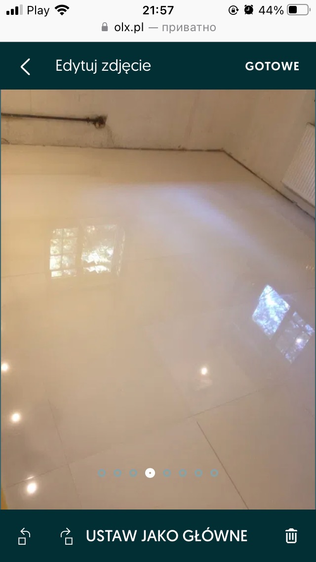 Błyszcząca, świeżo ułożona podłoga z jasnych paneli, odbijająca światło okna, widoczne łączenia paneli, surowy sufit z instalacją.