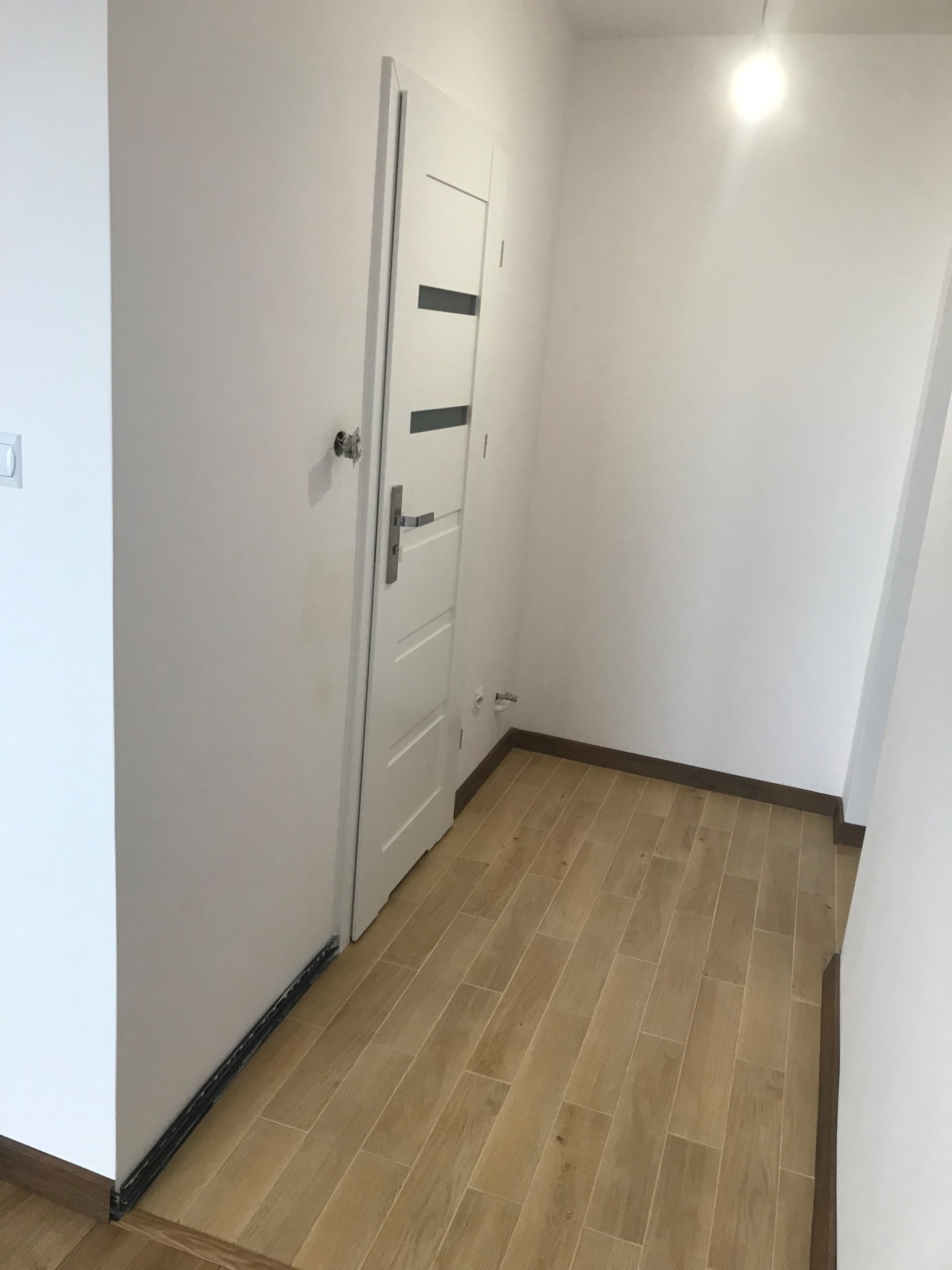 Wnętrze po remoncie: Świeżo pomalowane białe ściany, nowa podłoga z paneli imitujących drewno, białe drzwi wewnętrzne z szarymi akcentami.