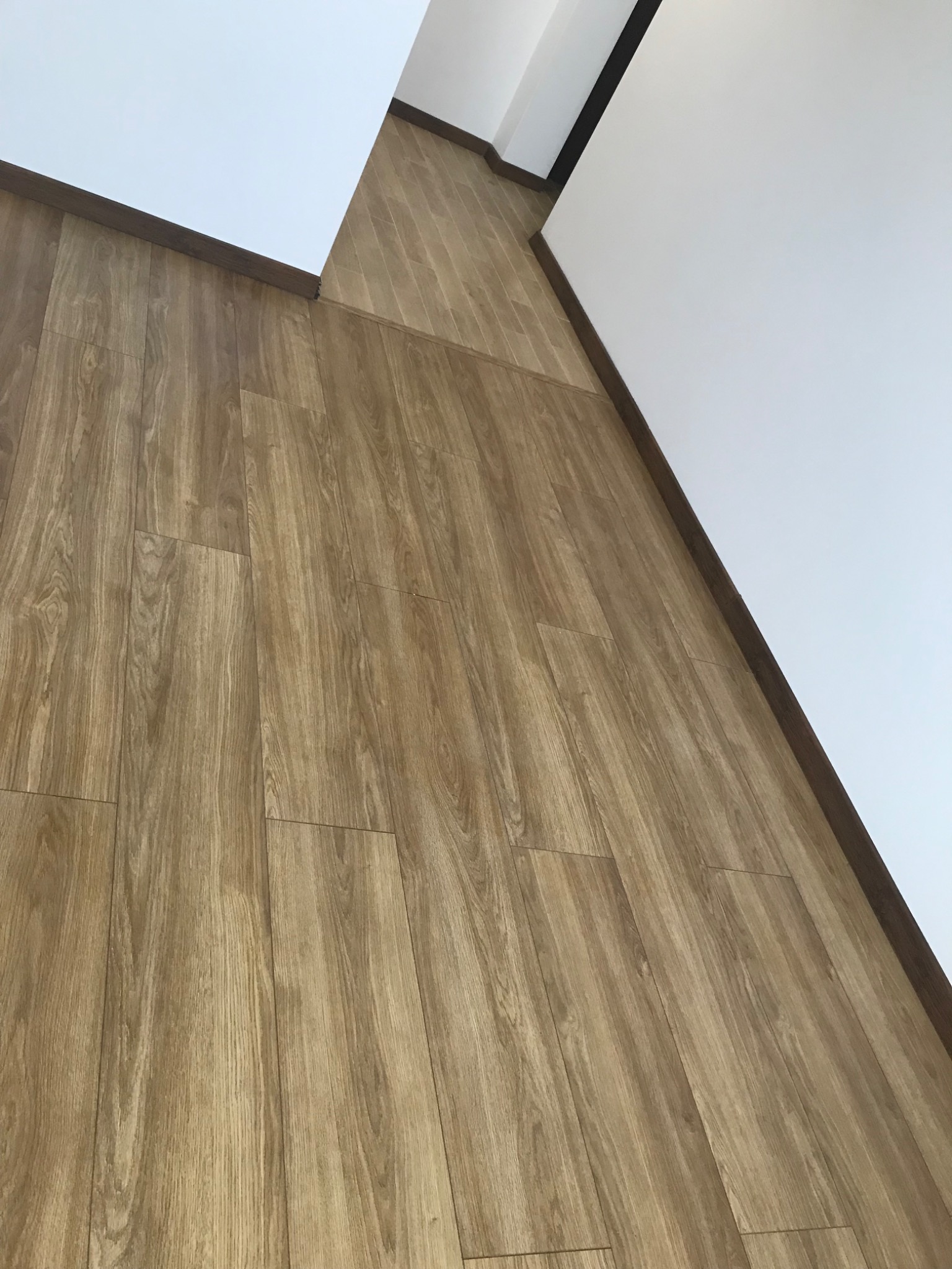 Ukończona podłoga z paneli winylowych w odcieniach drewna, z brązowymi listwami przypodłogowymi przy białych ścianach, widziana pod kątem.