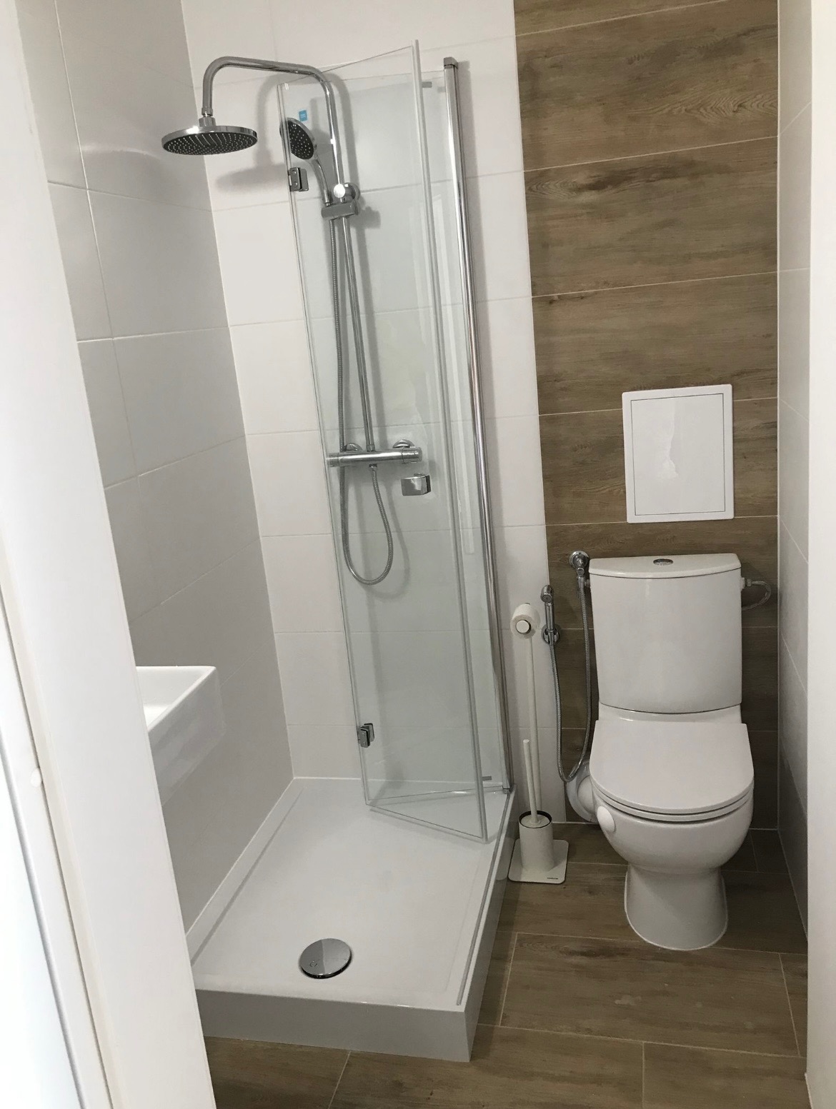 Nowoczesna łazienka z kabiną prysznicową typu walk-in, białą ceramiką i płytkami imitującymi drewno na ścianie.