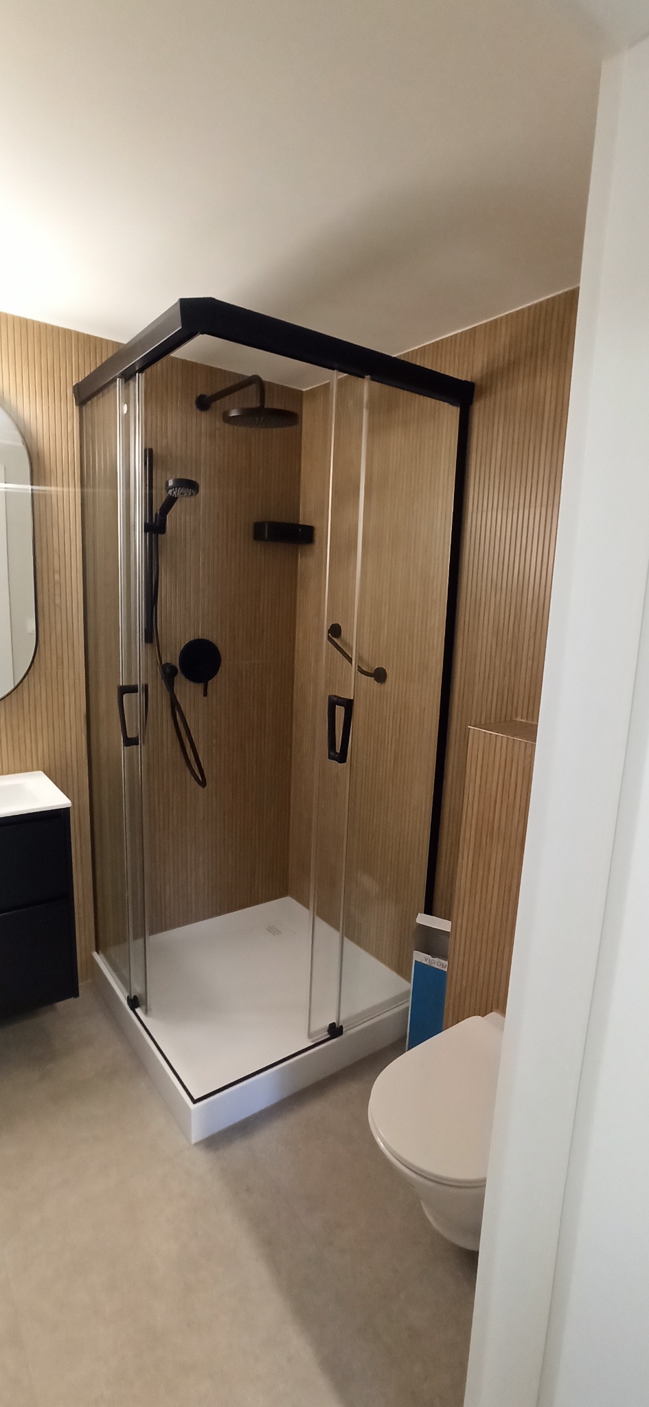 Nowoczesna kabina prysznicowa z czarnymi ramami i armaturą w łazience wykończonej panelami ściennymi imitującymi drewno.