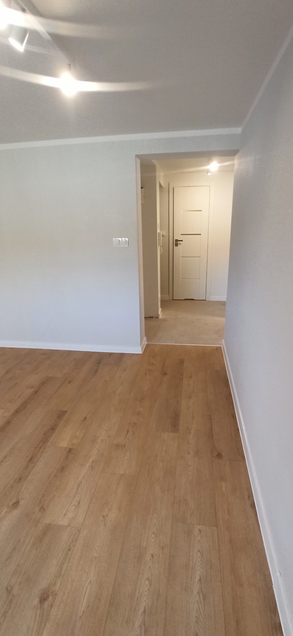 Jasne panele podłogowe w nowym mieszkaniu z białymi ścianami i drzwiami. Widok na korytarz z oświetleniem sufitowym.