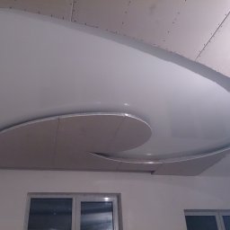 VIP Bud - Wykończony sufit napinany z elementami z płyty kartonowo-gipsowej tworzącymi dekoracyjny, spiralny wzór, widoczne okna w tle.