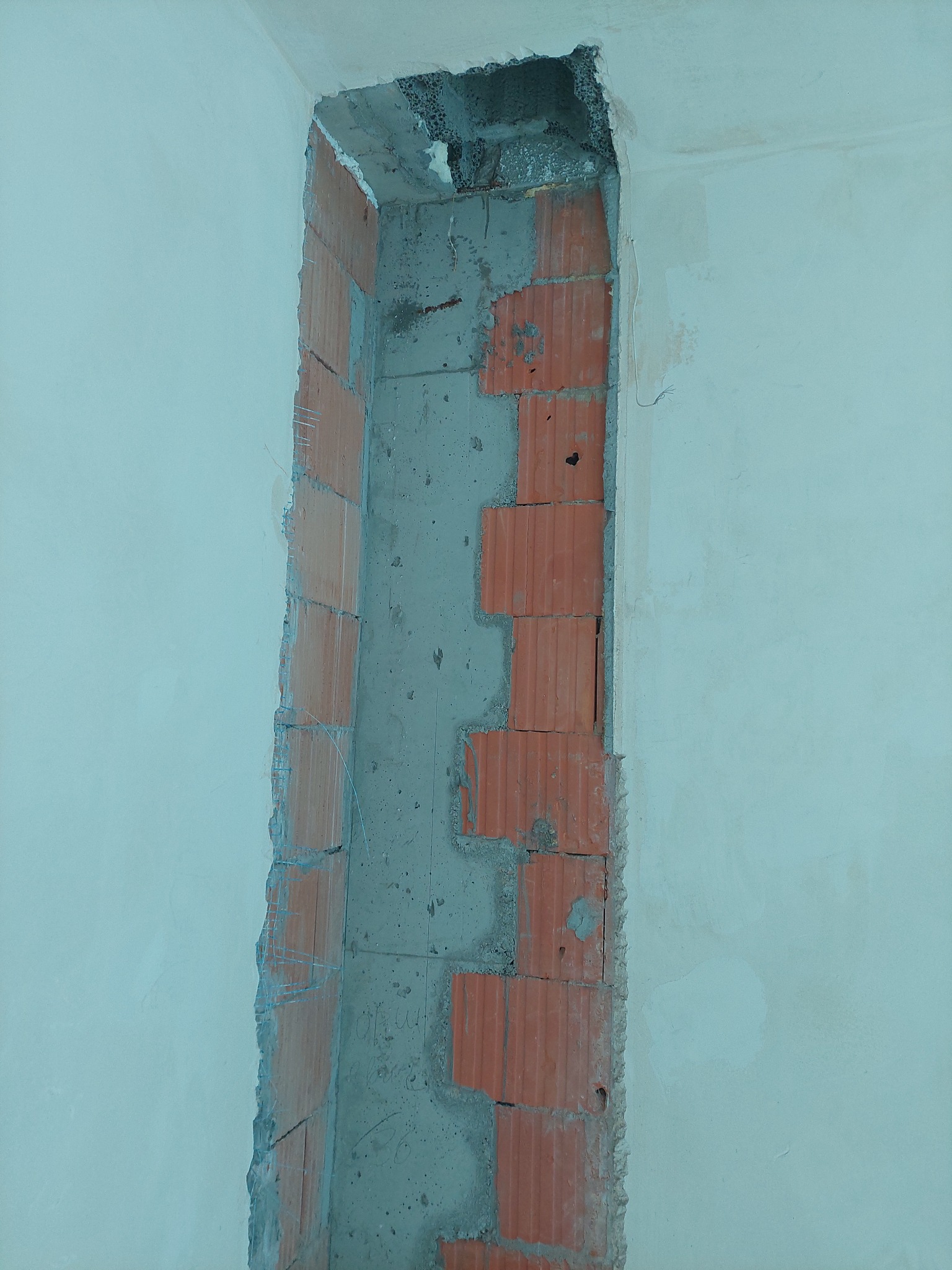 Otwór w ścianie przygotowany pod montaż ościeżnicy, widoczne cegły i fragmenty betonu, ściana o jasnym, pastelowym odcieniu.