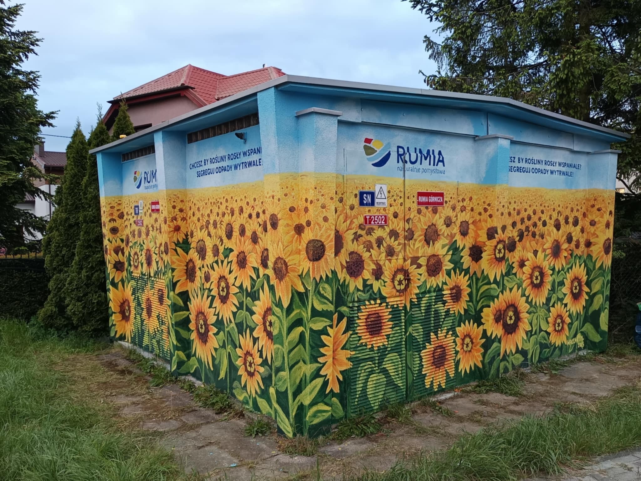 Transformator pomalowany w słoneczniki z hasłem o segregacji odpadów w Rumi. Mural z logiem miasta i napisem 'Rumia naturalnie pomysłowa'.