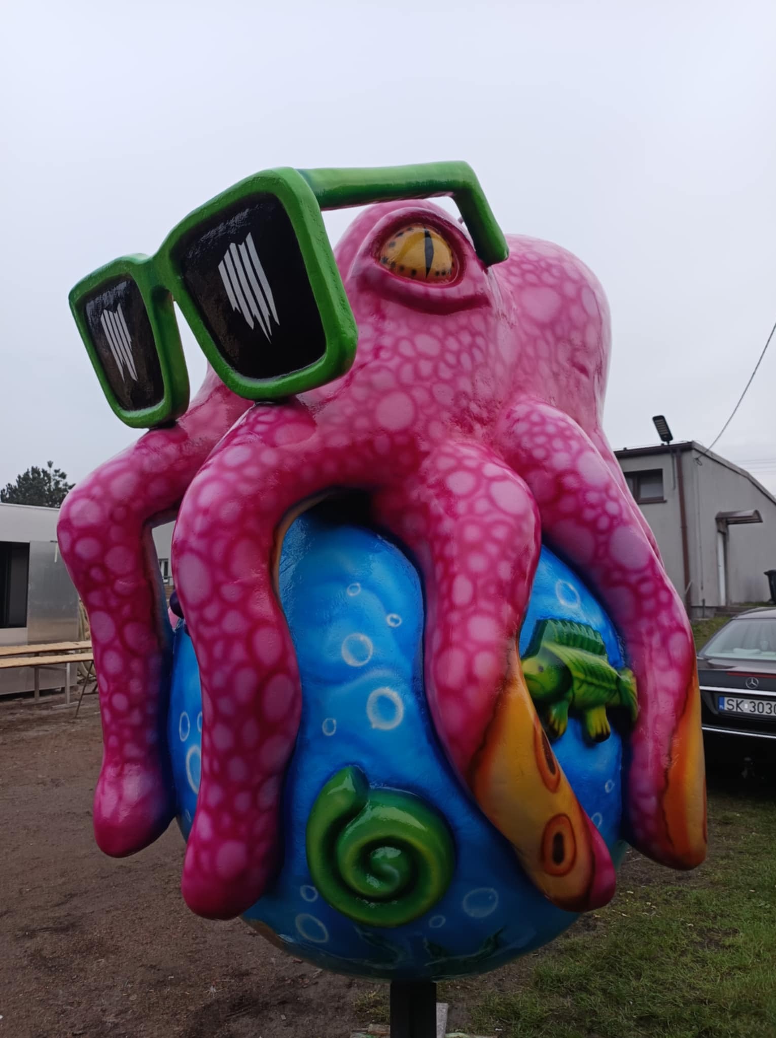 Ręcznie malowana, duża figura różowego ośmiornicy w zielonych okularach, siedzącej na niebieskiej kuli z morskimi motywami, na zewnątrz.