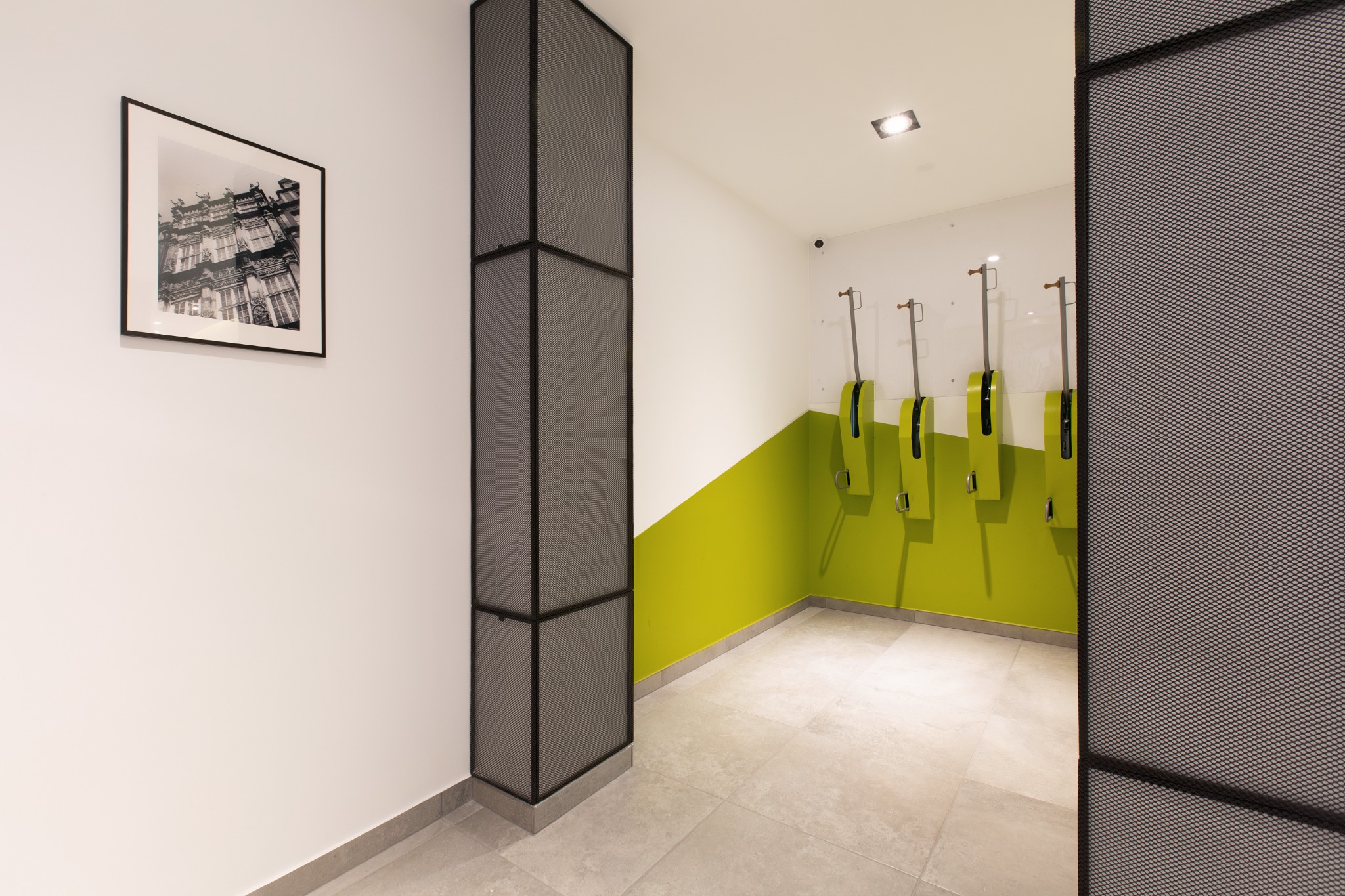 Nowoczesna toaleta publiczna z zielonym akcentem kolorystycznym, dozownikami mydła i czarno-białym zdjęciem budynku w ramce.