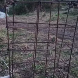 Szkielet z żebrowanej stali, prawdopodobnie zbrojenie pod fundament, ułożone na zewnątrz na trawie, widoczne elementy wiązania drutem.