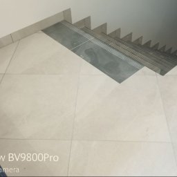 Fachowy Pracownik Budowlany - Wyłożone jasnymi płytkami podłoga i schody z ciemnymi płytkami antypoślizgowymi na stopniach, widok z góry, lekko zniekształcony przez obiektyw aparatu