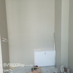 Fachowy Pracownik Budowlany - Świeżo pomalowane wnętrze z widoczną skrzynką elektryczną i wystającymi przewodami, przygotowane do dalszych prac wykończeniowych.