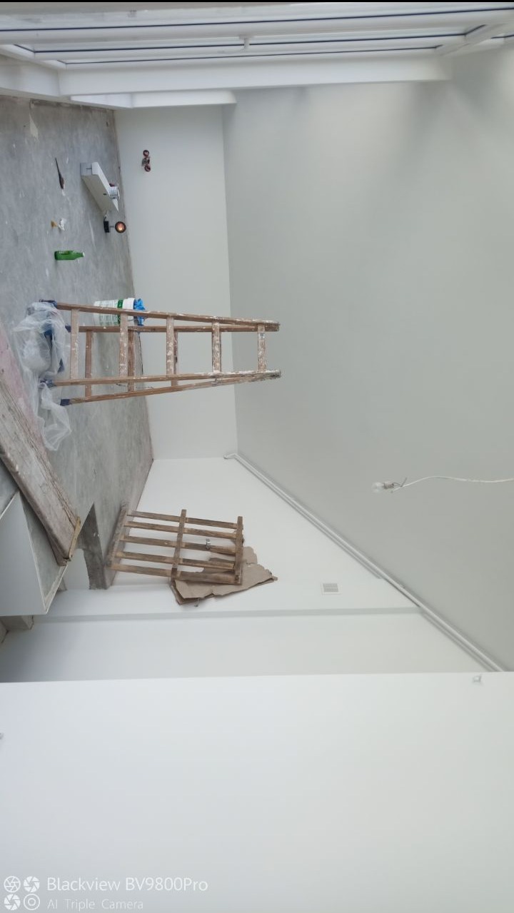 Wnętrze w trakcie odświeżania: drewniana drabina oparta o świeżo pomalowaną, białą ścianę, zabezpieczona folią podłoga, widoczne ślady po pracach malarskich.