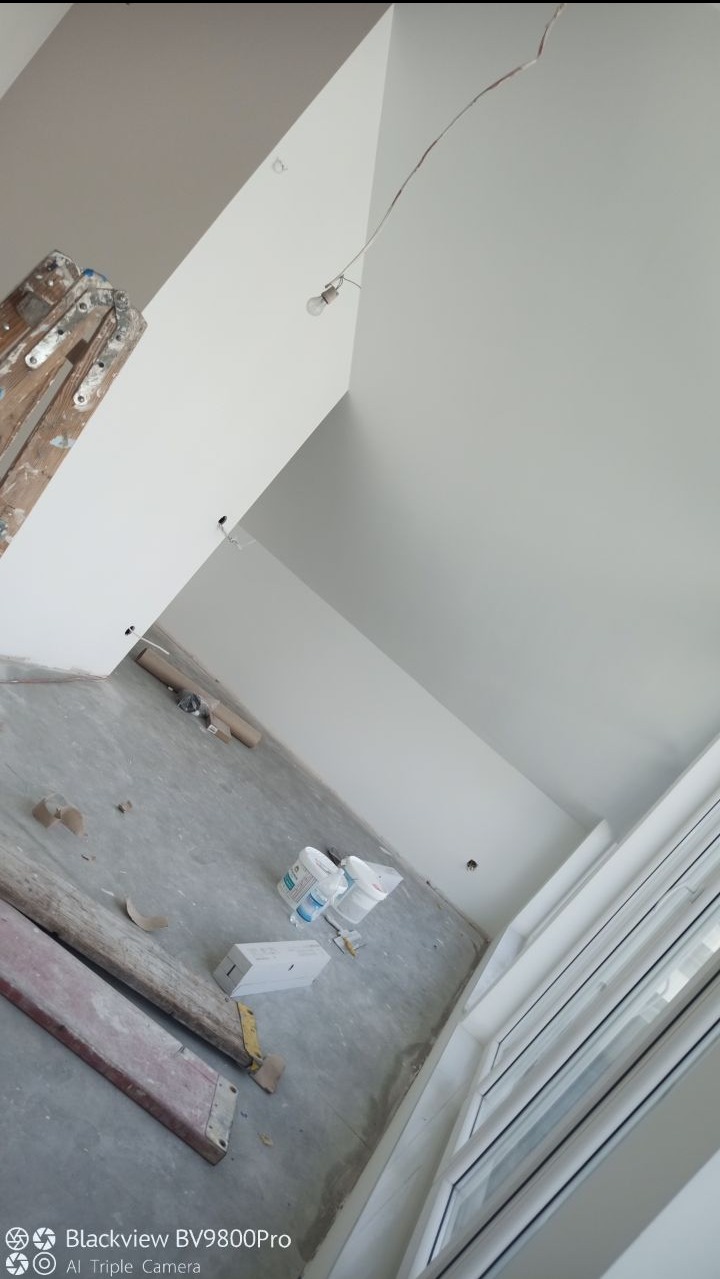 Wnętrze w trakcie odświeżania: pomalowane na biało ściany, sufit ze skosem, drabina malarska, puszki z farbą i surowa żarówka na kablu.