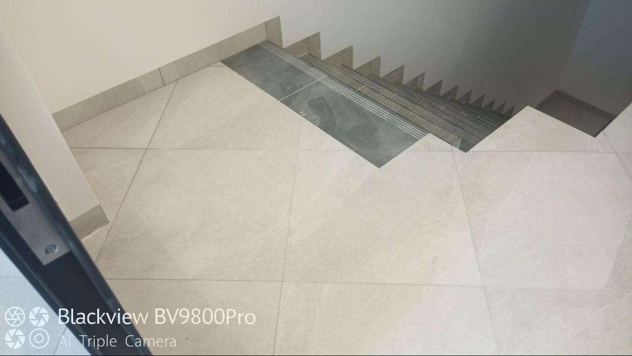 Wyłożone jasnymi płytkami podłoga i schody z ciemnymi płytkami antypoślizgowymi na stopniach, widok z góry, lekko zniekształcony przez obiektyw aparatu