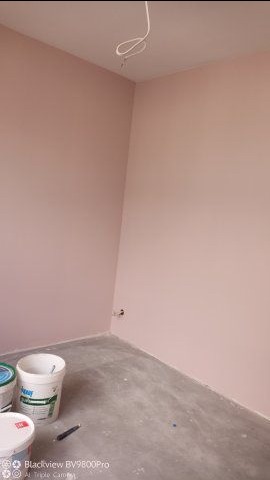 Świeżo pomalowane na różowo ściany pokoju, widoczne dwa wiadra z farbą i kabel wystający z sufitu.