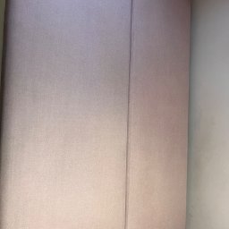 Piorex - Pranie tapicerki meblowej i samochodowej - Fragment jasnoróżowej, dwuczęściowej kanapy z wyraźnym szwem pośrodku, widok z góry, z fragmentem białego stelaża w dolnym rogu.