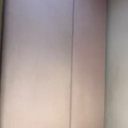 Fragment jasnoróżowej, dwuczęściowej kanapy z wyraźnym szwem pośrodku, widok z góry, z fragmentem białego stelaża w dolnym rogu.