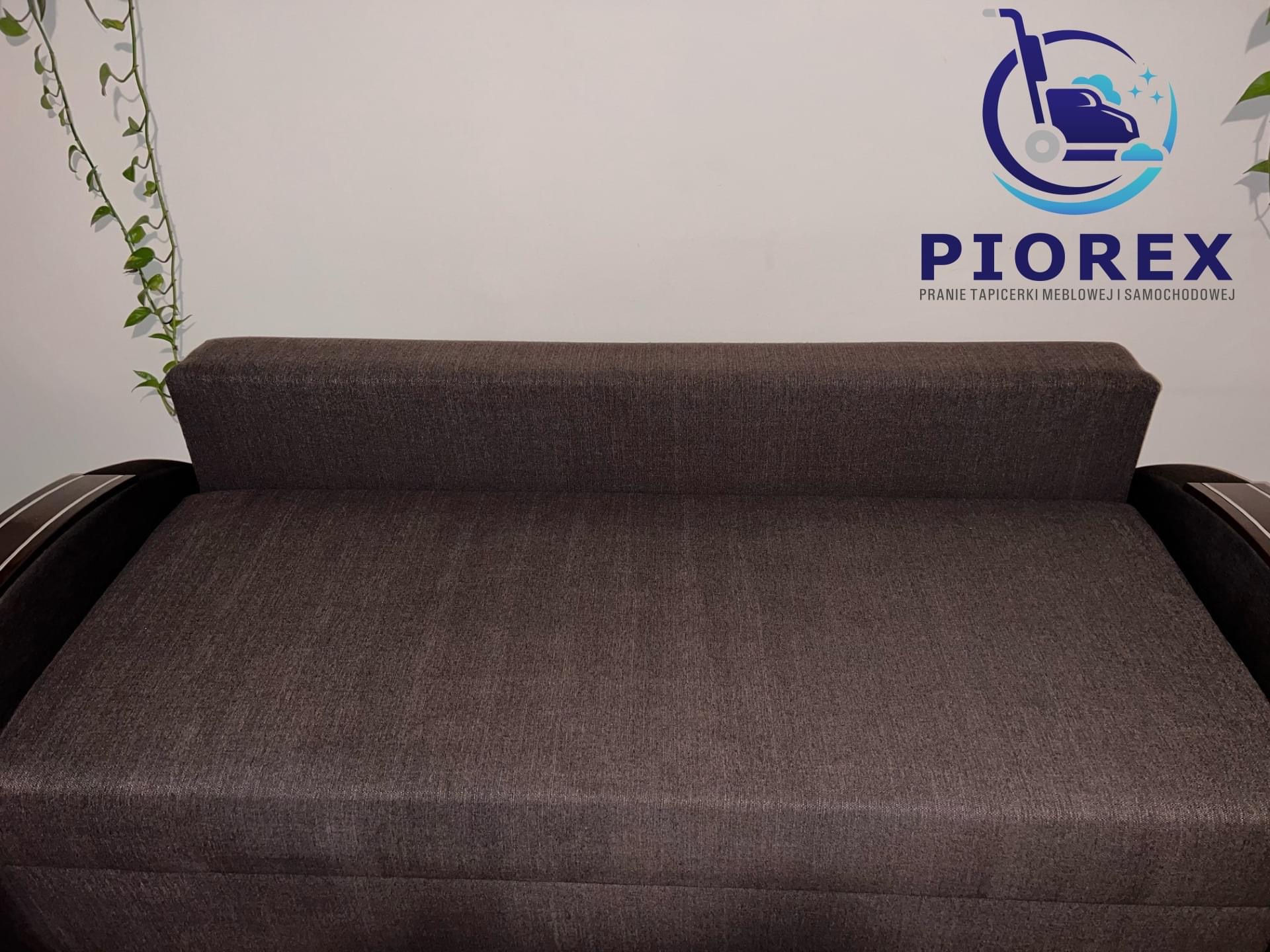 Brązowa, rozłożona kanapa z widocznym logo firmy oferującej usługi czyszczenia tapicerki meblowej i samochodowej na ścianie w tle.