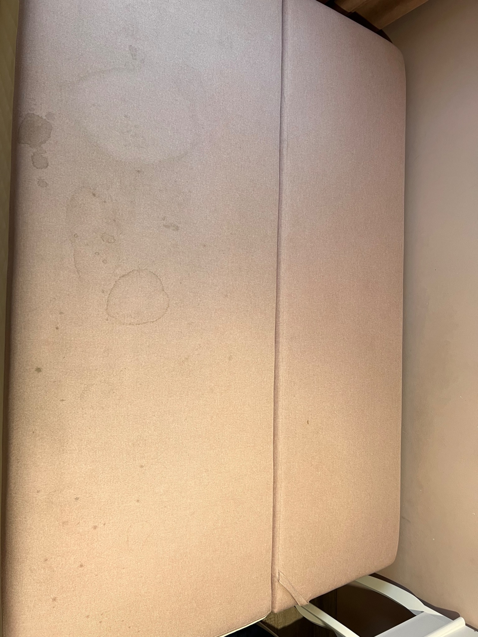 Fragment jasnoróżowej kanapy z widocznymi plamami i zabrudzeniami, ujęcie z góry.