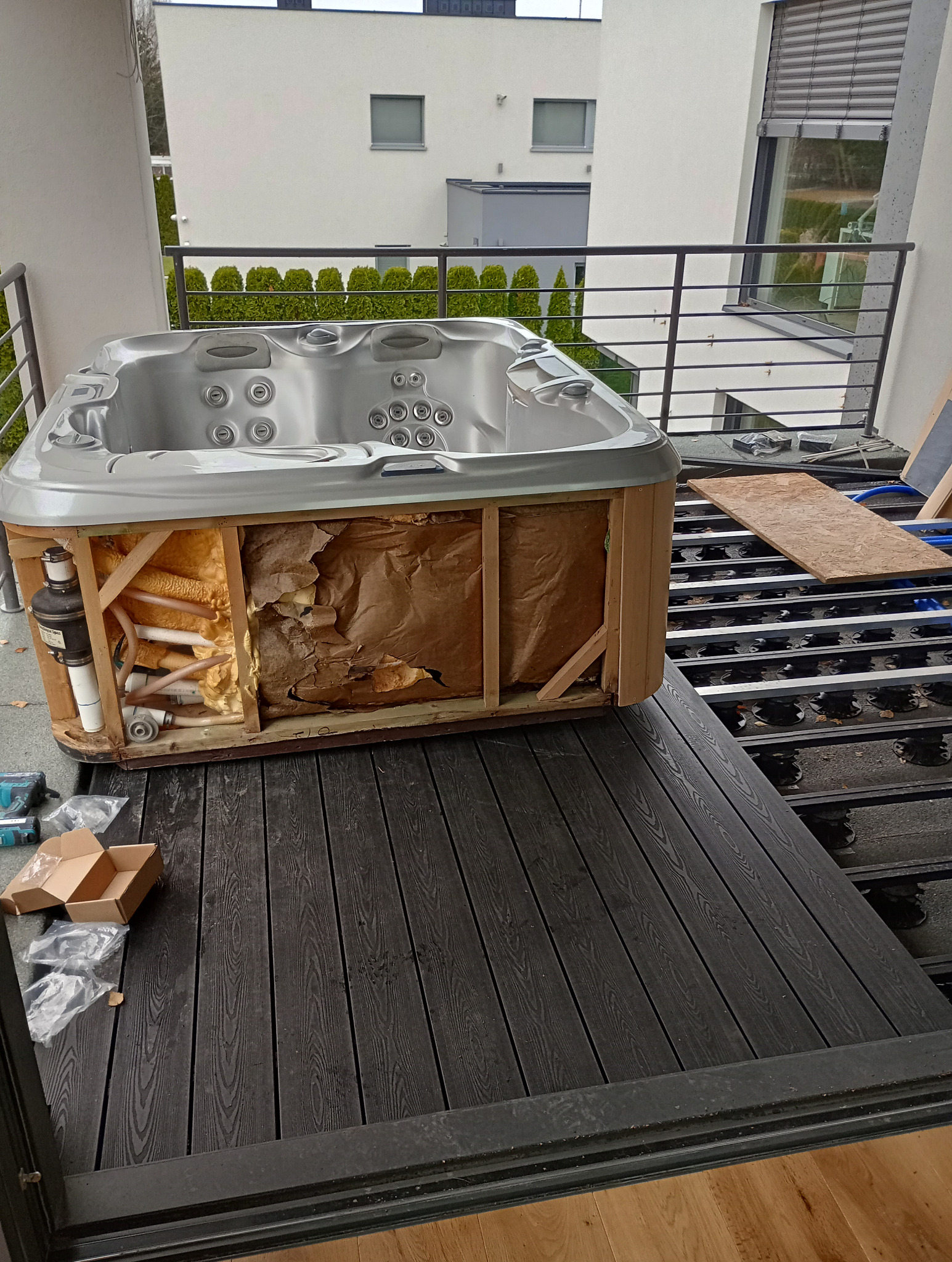 Montaż wanny spa na balkonie: widoczna konstrukcja wanny z instalacją, częściowo usunięta izolacja, czarne deski tarasowe i elementy konstrukcyjne pod spodem.