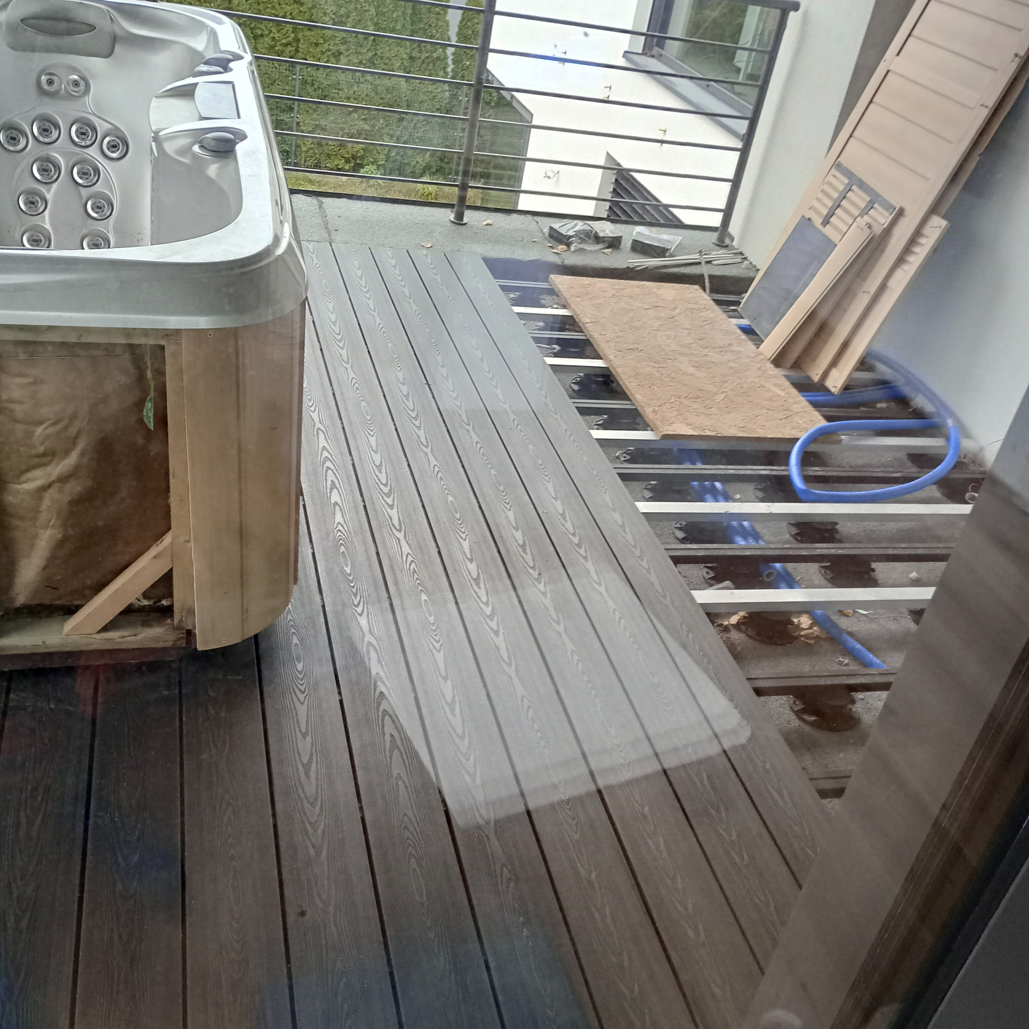 Montaż desek kompozytowych na tarasie z jacuzzi, widoczne elementy konstrukcyjne i niebieskie rury instalacji.