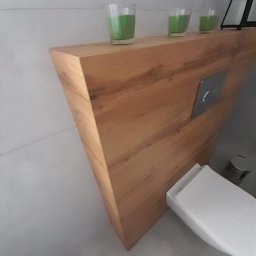 Łukasz Kaszuba - Trójkątna, dębowa półka w toalecie w Kiełpinie, z trzema świecami w szklanych pojemnikach na górze, zamontowana nad spłuczką.