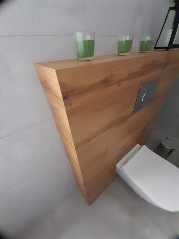 Trójkątna, dębowa półka w toalecie w Kiełpinie, z trzema świecami w szklanych pojemnikach na górze, zamontowana nad spłuczką.