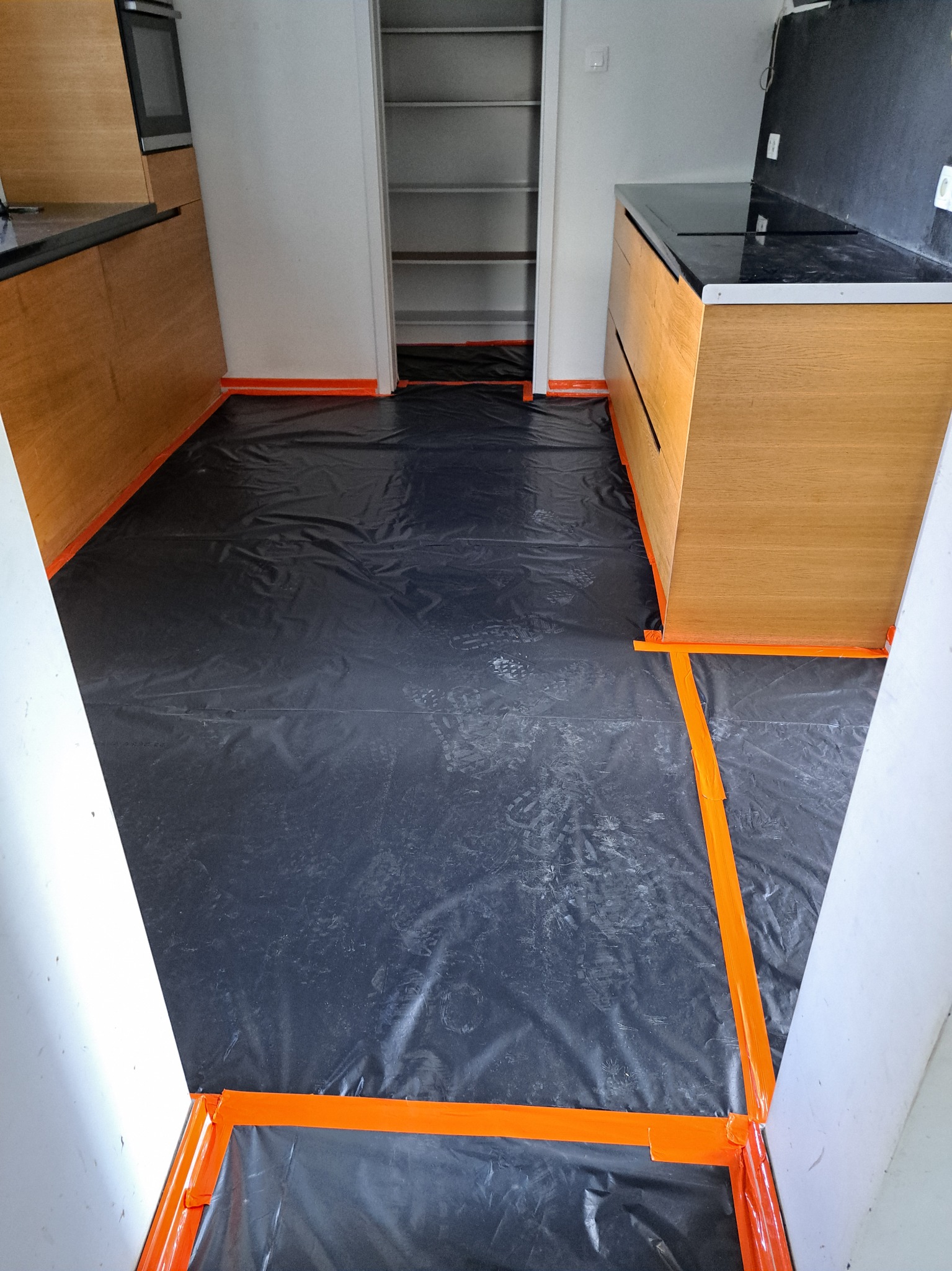 Kuchnia w trakcie zabezpieczania przed remontem: podłoga i meble kuchenne zakryte folią ochronną i taśmą malarską w kolorze pomarańczowym.