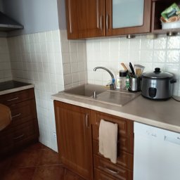 Euro Cleaning Olha Ivanenko - Umyta, czysta kuchnia z brązowymi szafkami, białymi płytkami i sprzętami AGD. Na blacie stoi srebrny garnek elektryczny i przybory kuchenne. W tle widać okap.