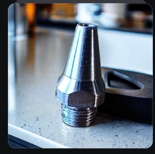 Chromowana dysza metalowa z gwintem, widoczna na jasnym blacie, z delikatnym odbiciem światła.