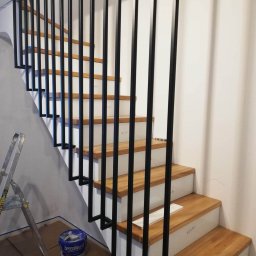 MAROBUD Marek Furtak - Schody drewniane z białymi podstopnicami i czarną, minimalistyczną balustradą, widoczne ślady prac malarskich, drabina i puszka farby Speedmaster w tle.