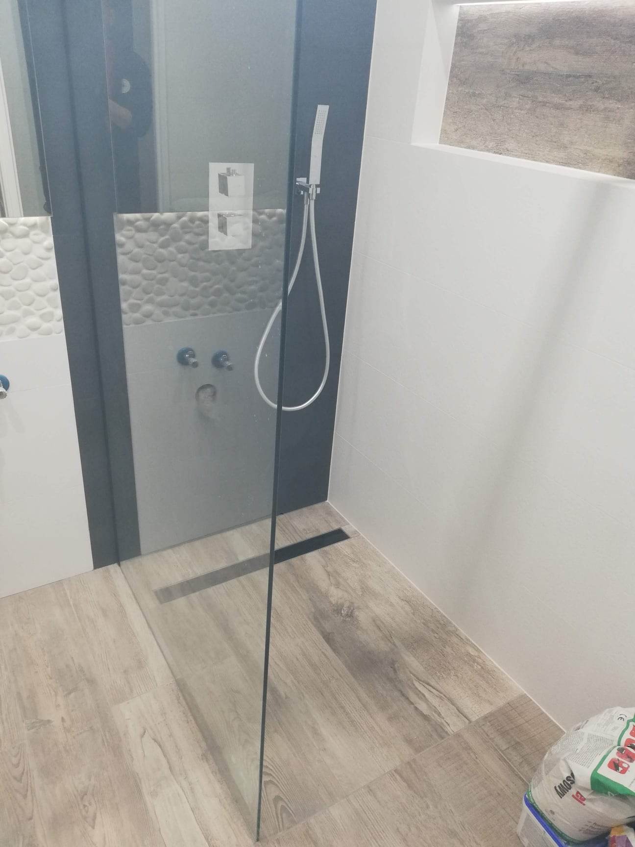 Nowoczesna kabina prysznicowa z deszczownicą, wykończona płytkami imitującymi drewno i mozaiką kamienną, z odpływem liniowym w podłodze.