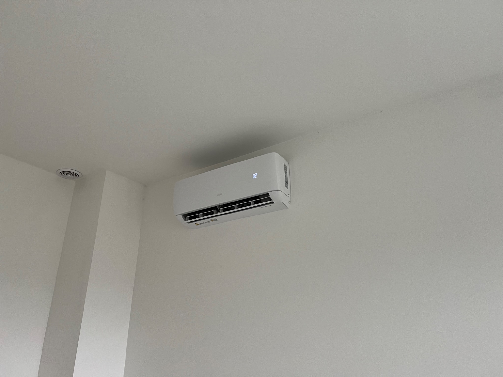 Biały klimatyzator ścienny z wyświetlaczem temperatury 32 stopnie Celsjusza, zamontowany w jasnym, minimalistycznym wnętrzu.