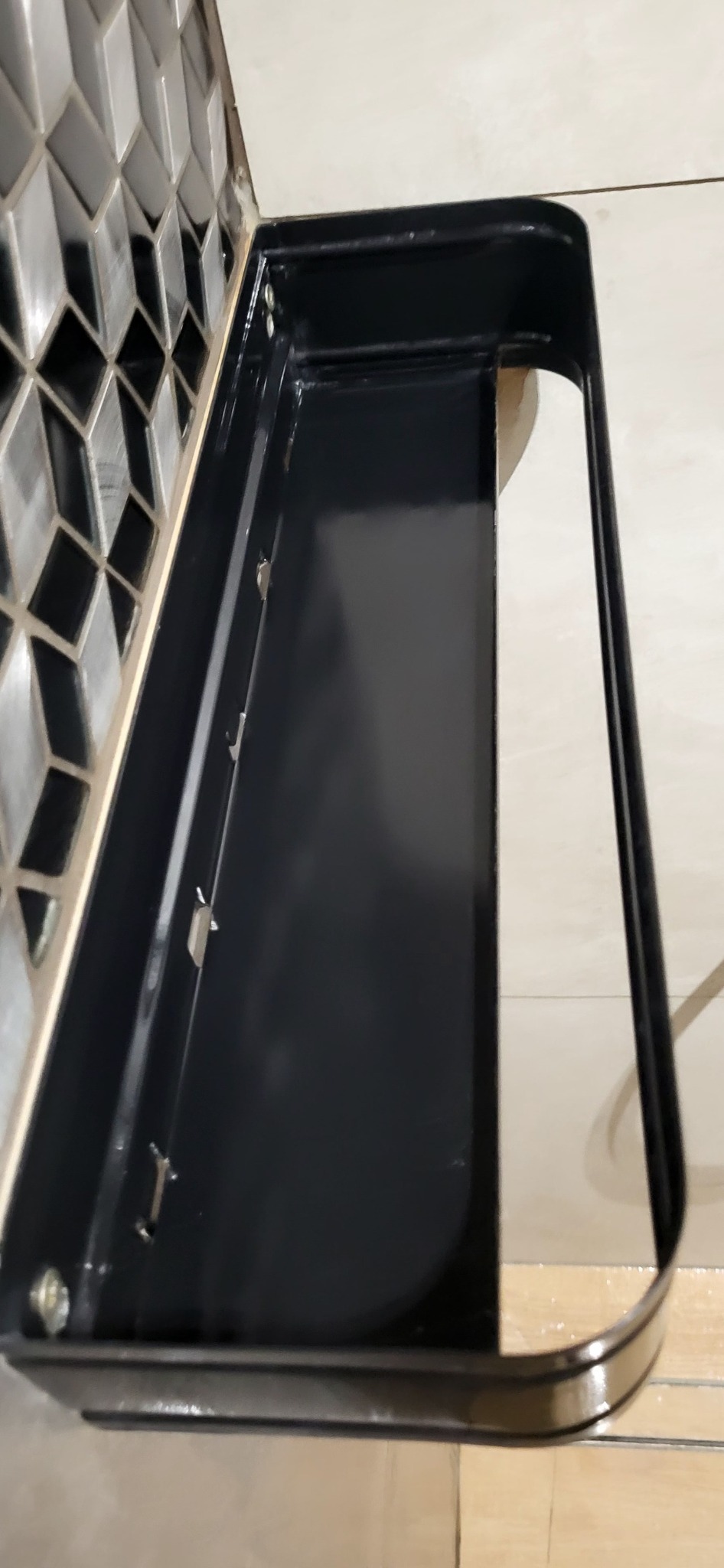 Półka łazienkowa w kolorze czarnym, zamontowana na ścianie z dekoracyjnymi płytkami, widok z góry.