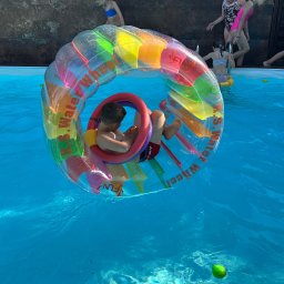 Biuro Turystyczne Skaut Tour sp. z o. o. - Chłopiec w kolorowym, dmuchanym kole wodnym w basenie; dzieci w tle, letnia zabawa na imprezie integracyjnej z animacjami wodnymi.