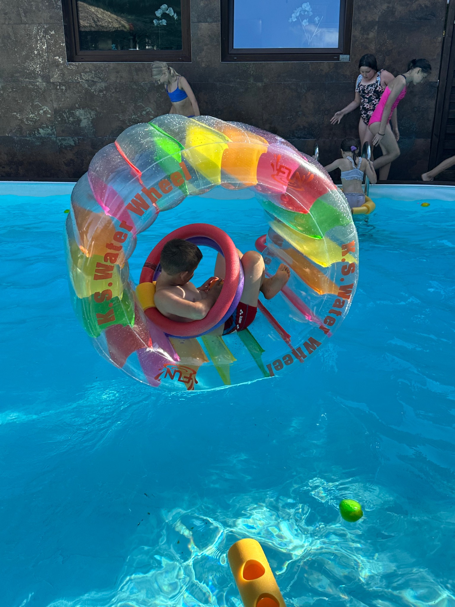 Chłopiec w kolorowym, dmuchanym kole wodnym w basenie; dzieci w tle, letnia zabawa na imprezie integracyjnej z animacjami wodnymi.