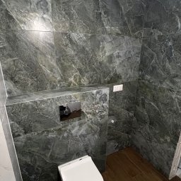 MC Design Jakub Ciuńczyk - Wykończona łazienka z płytkami imitującymi zielony marmur na ścianach, podwieszana toaleta i drewnopodobną podłogą.