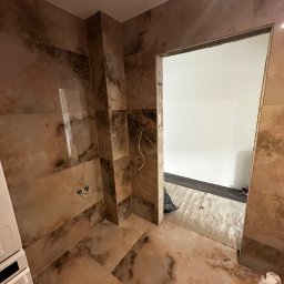 MC Design Jakub Ciuńczyk - Wnętrze łazienki w trakcie remontu z położonymi płytkami imitującymi marmur na ścianach i podłodze, widoczne wyprowadzone kable i niezabezpieczony otwór drzwiowy.