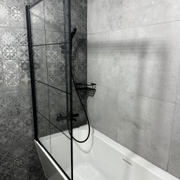 MC Design Jakub Ciuńczyk - Nowoczesna łazienka z białą wanną i szklanym parawanem w czarnej ramie, szare płytki z wzorem i deszczownica.