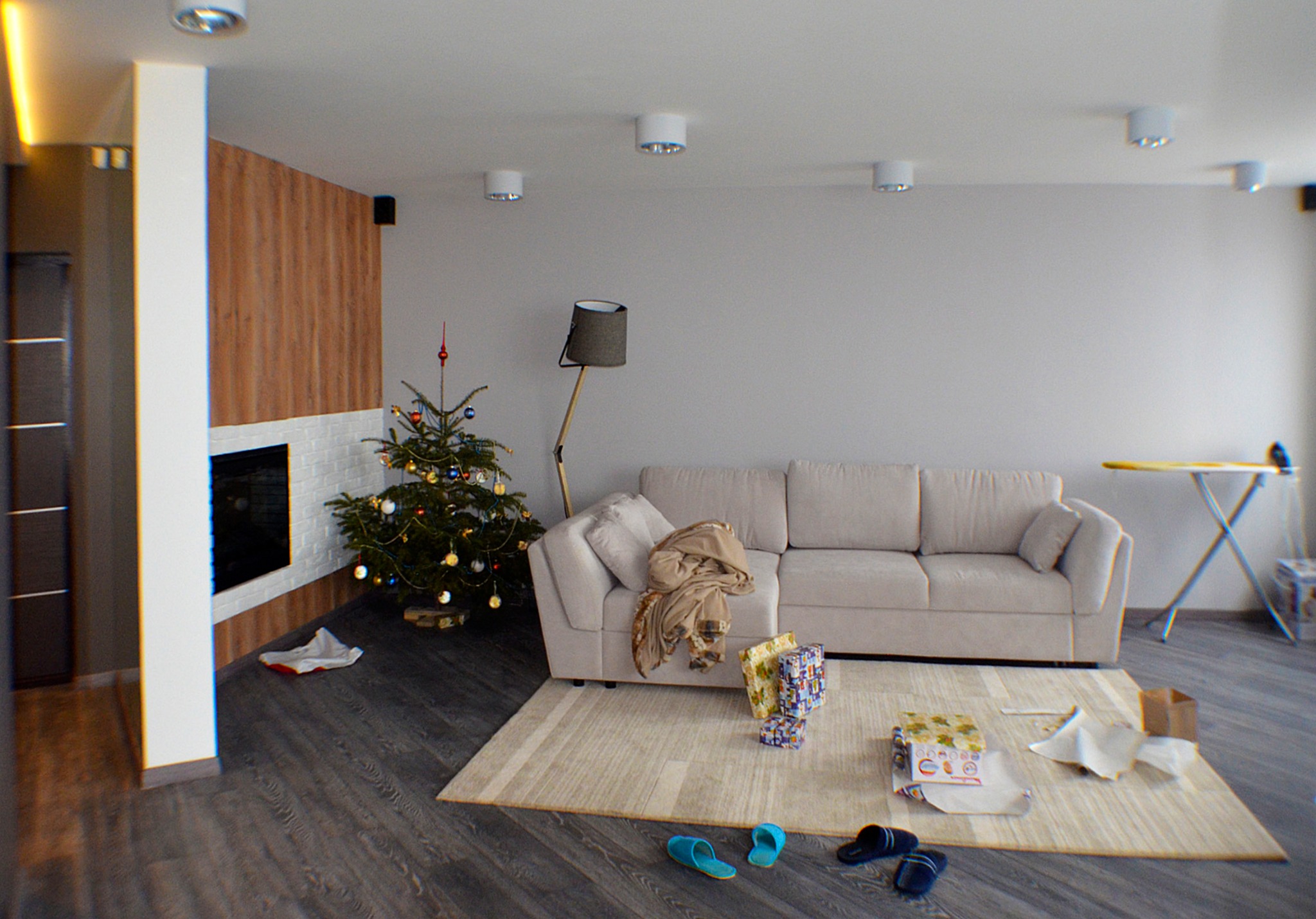 Jasne wnętrze salonu z choinką, kremową sofą, dywanem w paski i elementami dekoracyjnymi z bożonarodzeniowymi prezentami, widok na ścianę z drewnianą okładziną i kominkiem.