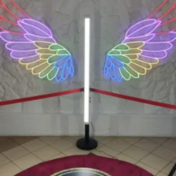 Oświetlona platforma obrotowa z neonowymi skrzydłami anioła w tle, otoczona czerwoną taśmą.