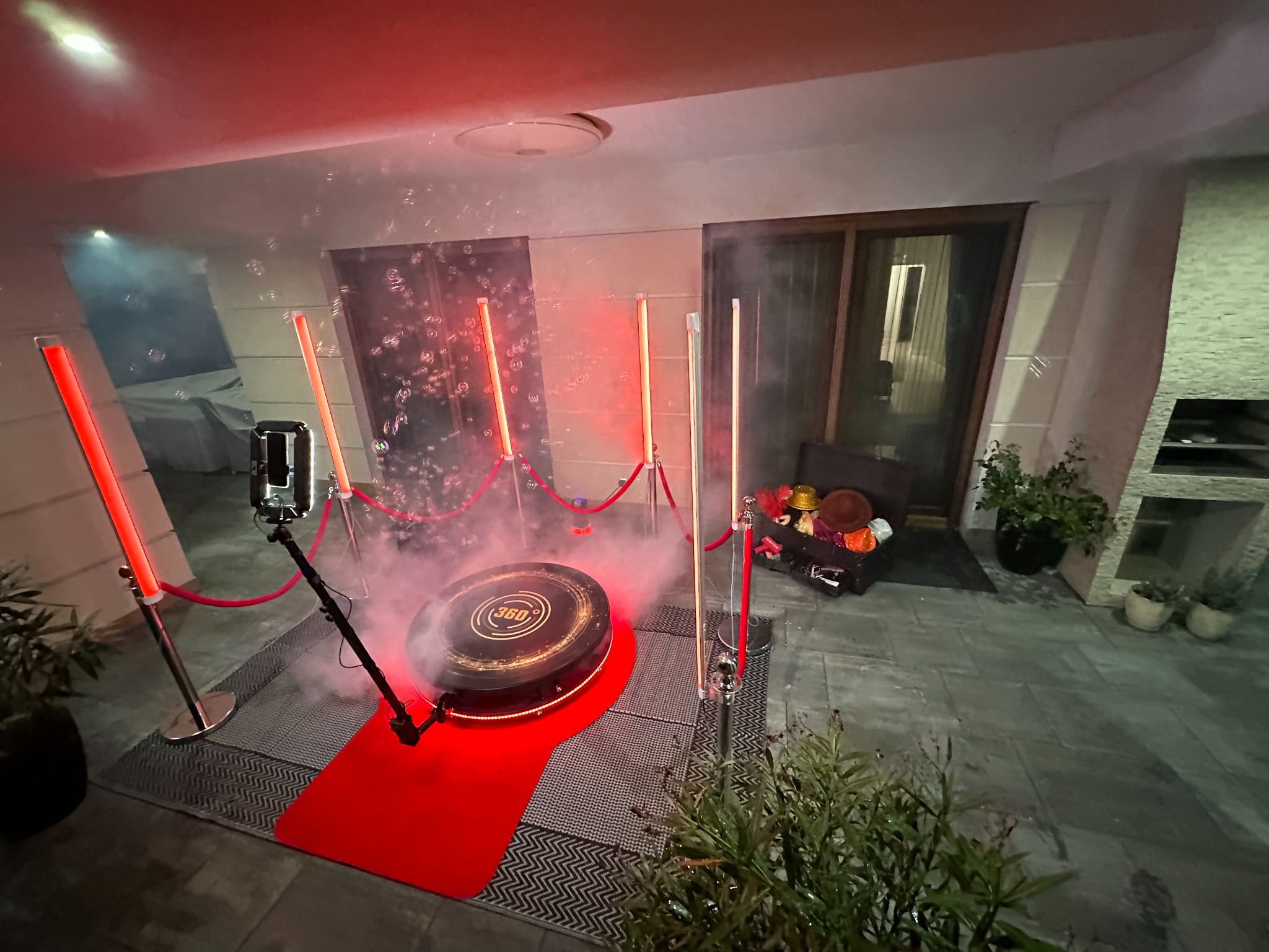 Oświetlona platforma obrotowa 360 stopni z czerwonym dywanem i barierkami, otoczona efektem dymu i bańkami mydlanymi, rekwizyty w tle.